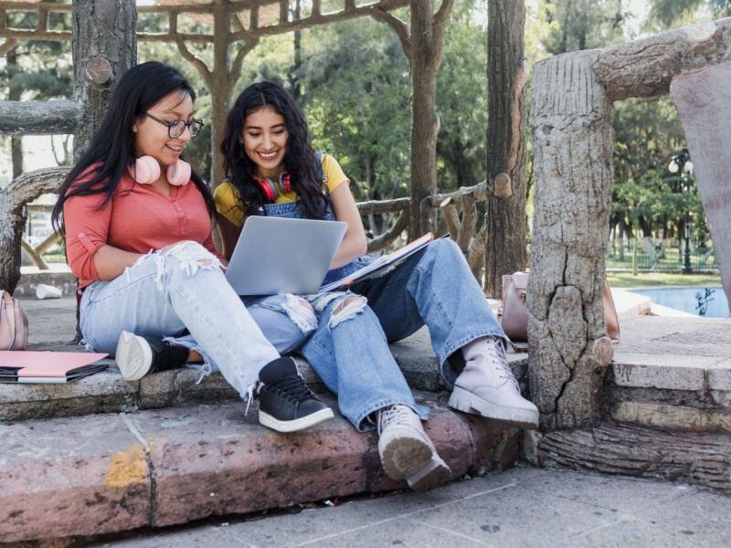 Dos estudiantes consultando información sobre la Convocatoria ECOEMS 2025 en una laptop al aire libre