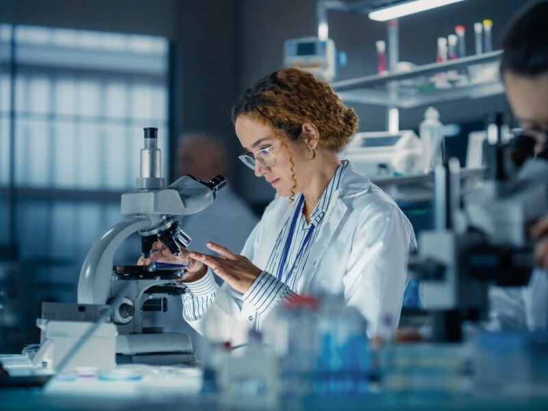 Investigadora en laboratorio analizando muestras biológicas con microscopio avanzado.