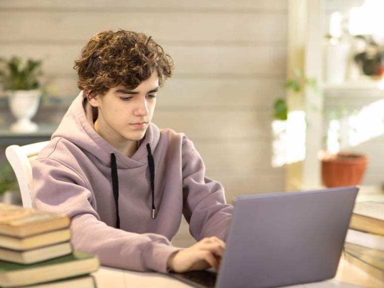 Adolescente utilizando un simulador ecoems en su computadora junto a libros de estudio.