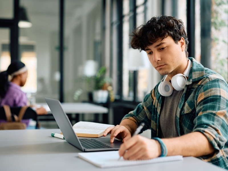 Estudiante con auriculares estudiando en línea en una biblioteca con su laptop.