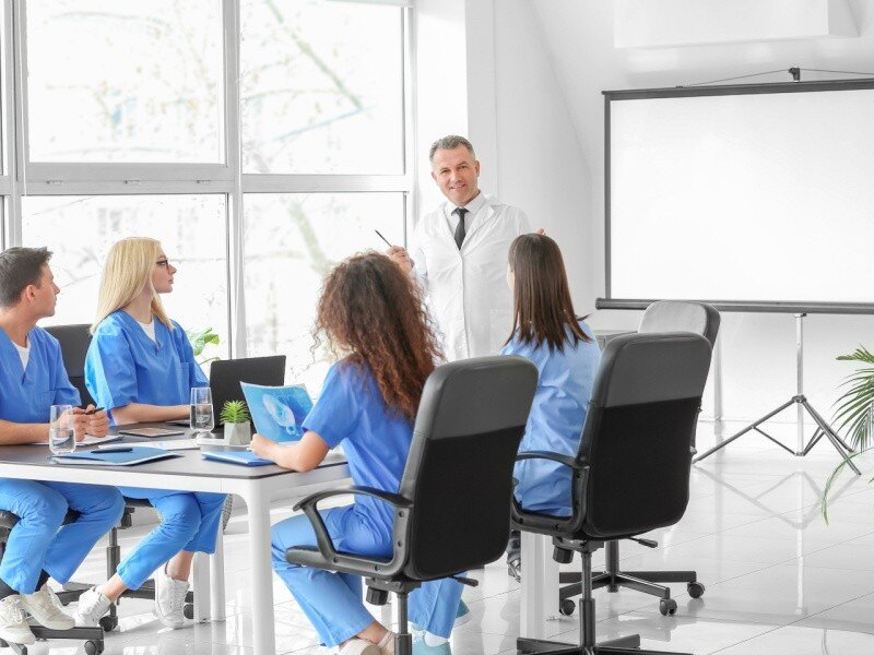 Grupo de médicos en una sesión de capacitación con un líder médico, destacando las oportunidades de gestión y liderazgo en el ámbito sanitario.