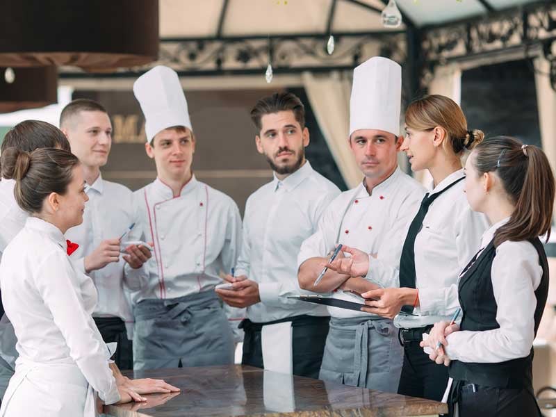 Gerente de restaurante interactuando con su equipo en la terraza del restaurante, demostrando liderazgo y atención al cliente en un entorno de hospitalidad.