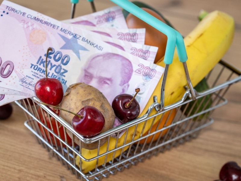 Carrito de compras miniatura lleno de alimentos y billetes de lira turca, simbolizando el impacto de la inflación en el poder adquisitivo.