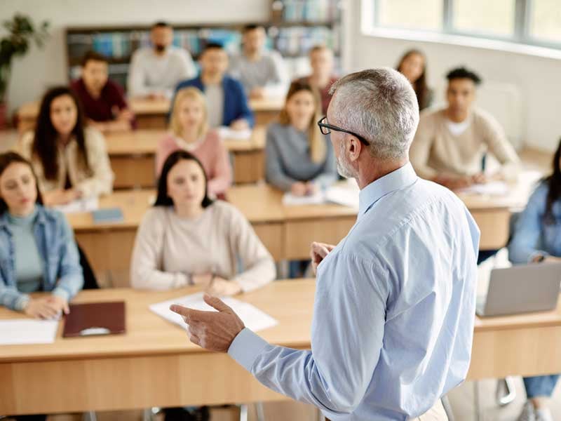 Profesor impartiendo clase a grupo de universitarios en aula, carrera para ser maestro en México
