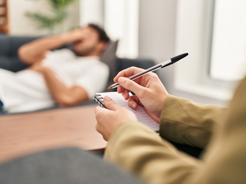 Psicólogo tomando notas mientras escucha a un paciente recostado, representando el psicoanálisis y los orígenes clínicos de la psicología