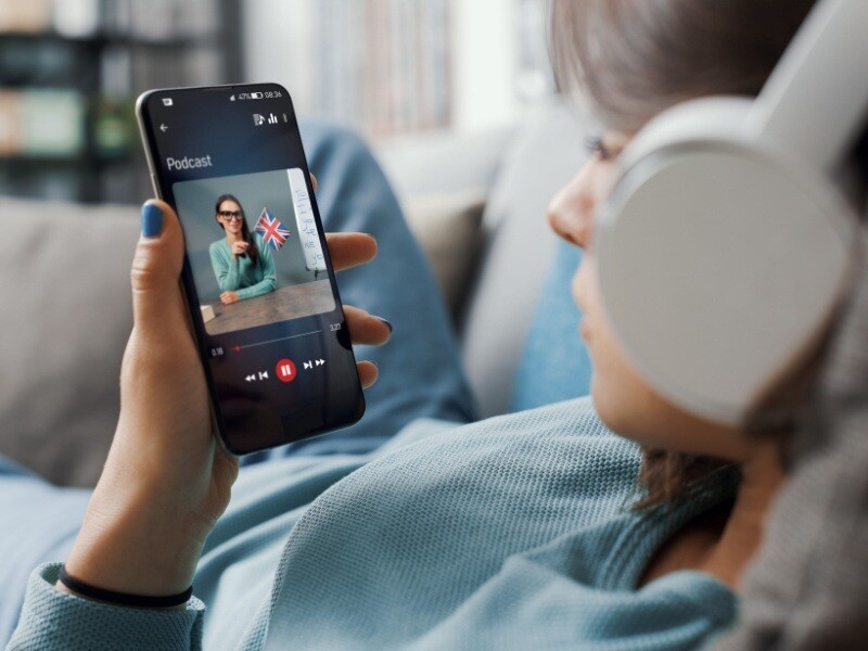 Mujer escuchando un podcast de inglés en su celular con auriculares, mostrando una forma moderna de aprender inglés online.