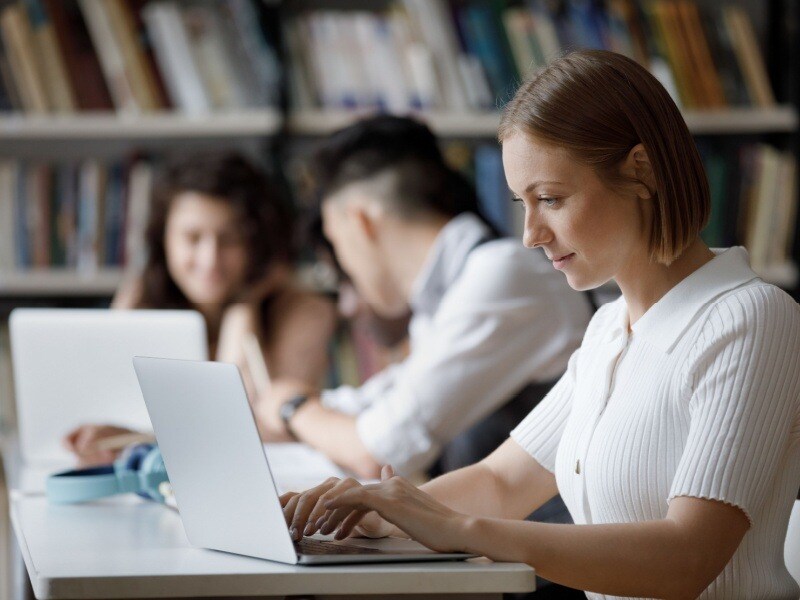 Estudiante en biblioteca trabajando en su laptop, simbolizando el aprendizaje continuo a través de diplomados o certificaciones.