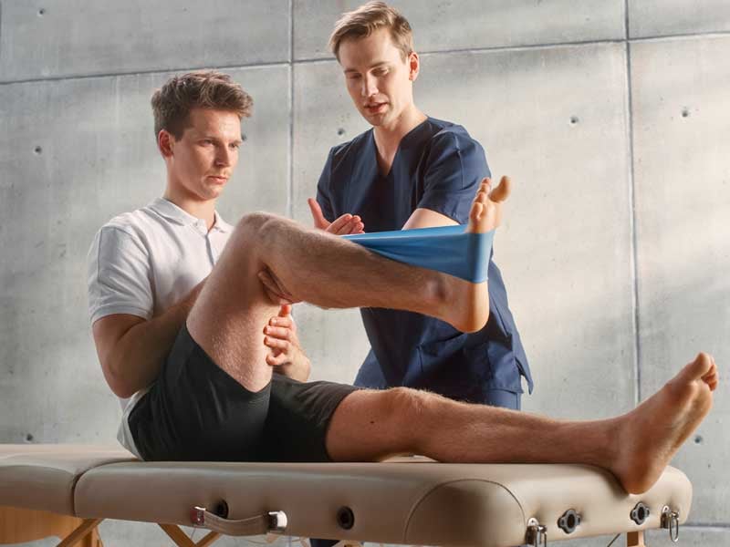 Fisioterapeuta deportivo demostrando técnicas de estiramiento a un paciente joven en una clínica de rehabilitación