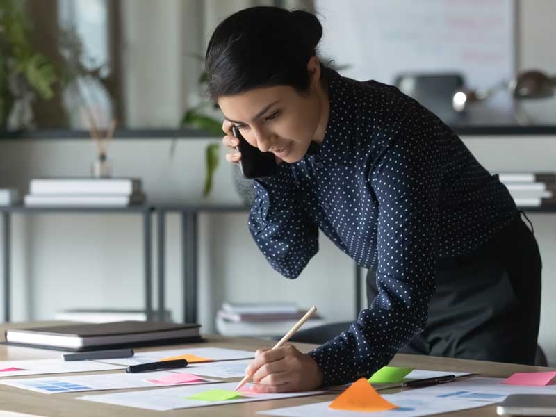 Mujer profesional hablando por teléfono y tomando notas en una oficina, ilustrando la organización y gestión de proyectos empresariales