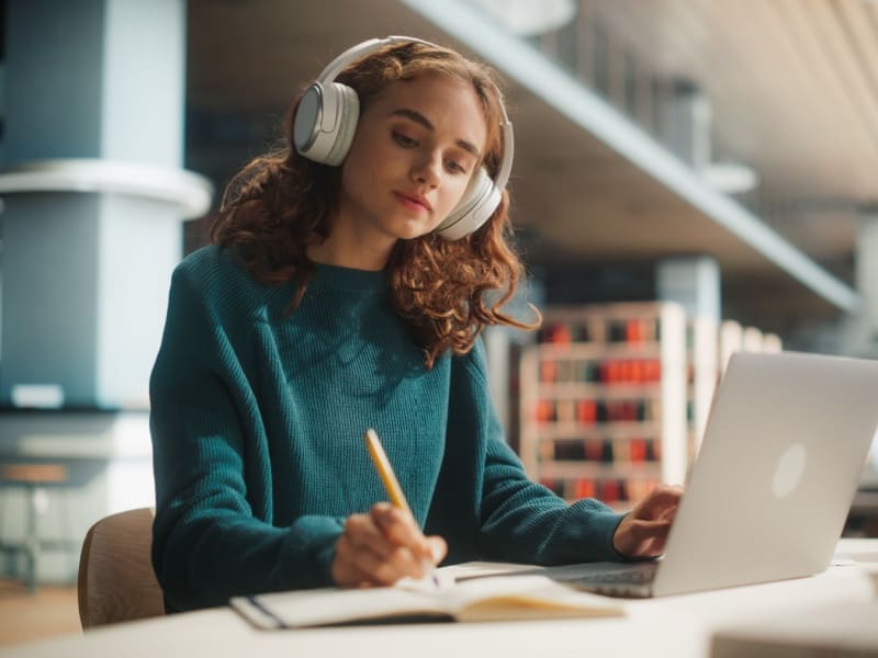 Estudiante con audífonos en biblioteca realizando microcredenciales