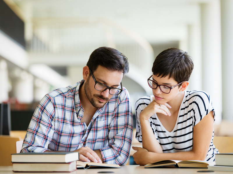 Dos estudiantes leyendo un libro en una biblioteca