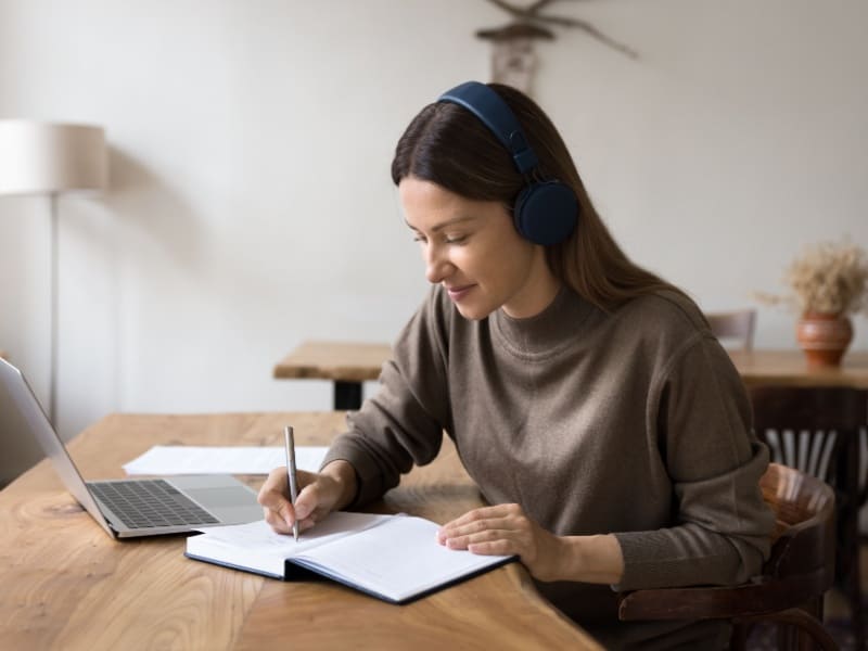 Mujer estudiando una maestría en línea desde casa, tomando notas frente a su laptop con audífonos, modalidad flexible para profesionistas en México.