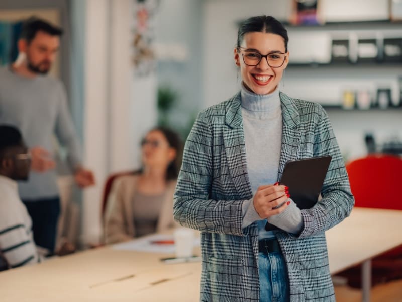 Mujer joven en oficina corporativa sosteniendo una tablet, representando el camino profesional de trabajar en una empresa.