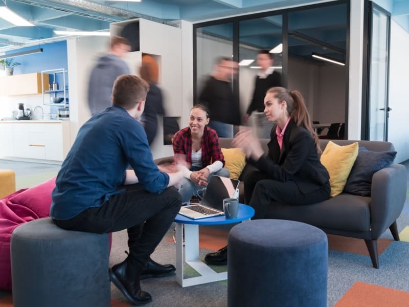 Personas jóvenes conversando en una oficina moderna, colaborando en equipo y analizando ideas de trabajo en un ambiente corporativo.