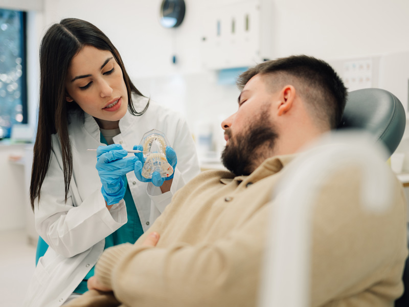 Dentista explicando tratamiento a paciente con modelo dental en consultorio moderno