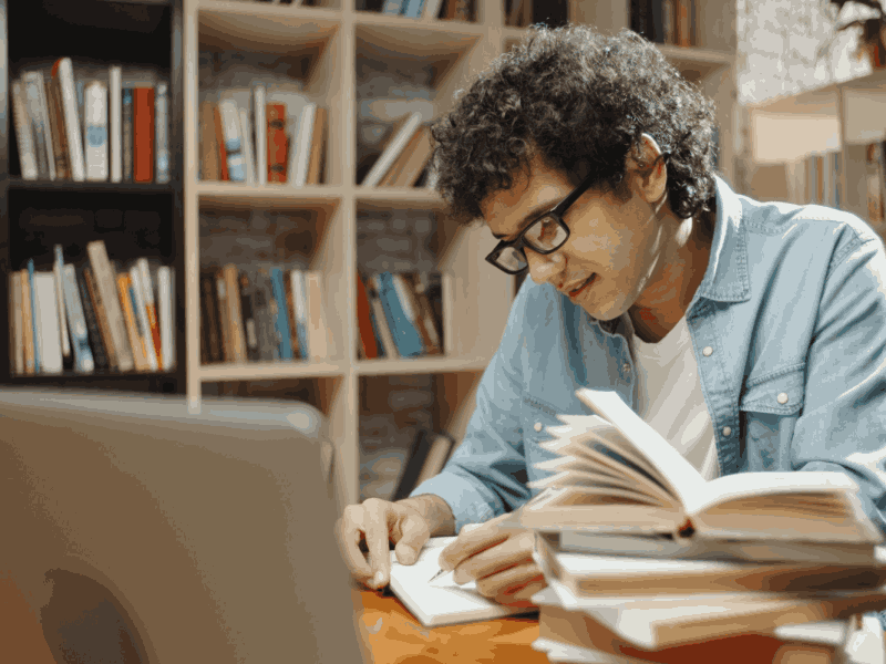  Alumno preparándose para el examen de admisión en la biblioteca con laptop y apuntes