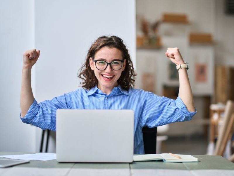 Estudiante universitaria celebra frente a su laptop tras completar su perfil de LinkedIn sin experiencia laboral