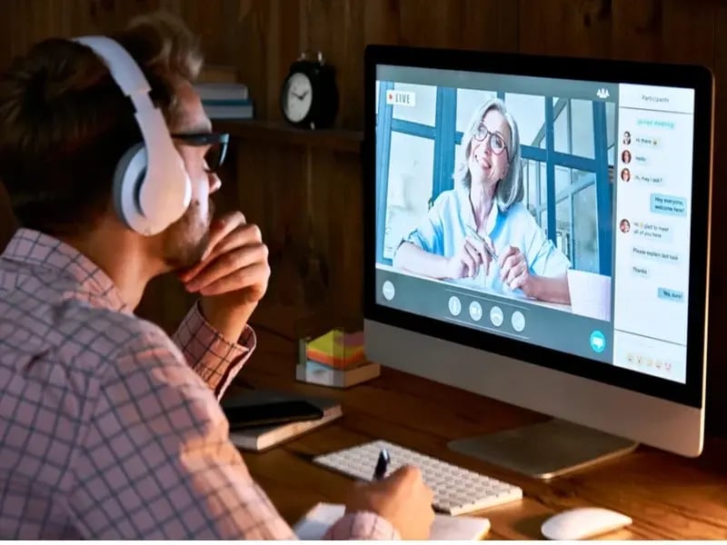 Hombre tomando una clase virtual en línea con una profesora en videollamada, como parte de una maestría.