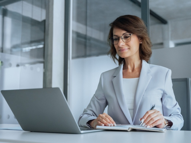 Mujer estudiando en laptop y tomando notas para una maestría UVM con Harvard Online