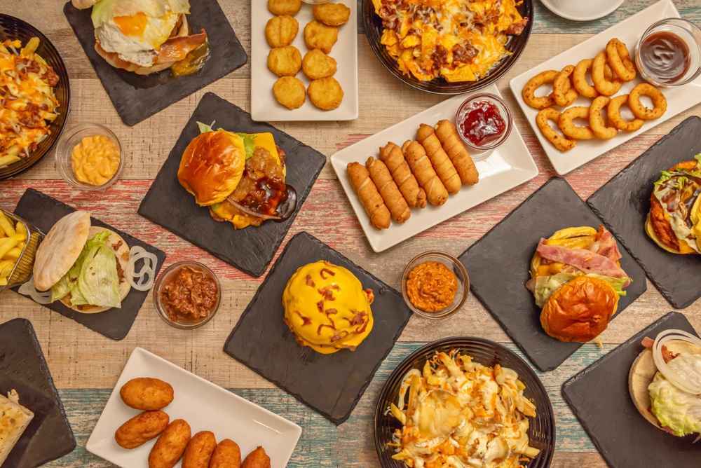 Variedad de platillos de comida rápida servidos en mesas de madera, representando la diversidad gastronómica y su impacto en la cultura contemporánea.